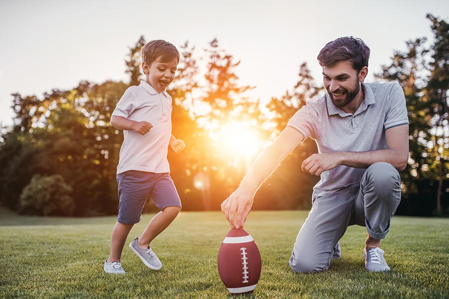 Personal Insurance - Father and Son Playing Football Together, Dad Holding the Ball for Little Boy to Kick